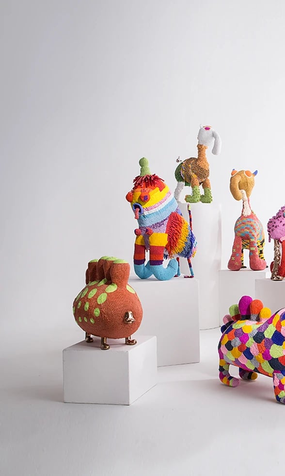 Colorful beaded sculptural creatures by the Haas Brothers, arranged on white plinths — left view